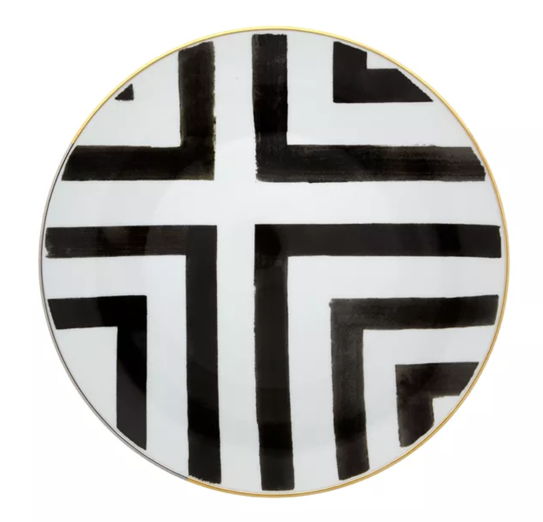 The Sol Y Sombra charger by Christian Lacroix x Vista Alegre is a round white porcelain plate with bold black intersecting lines and right angles, elegantly finished with a thin gold rim.