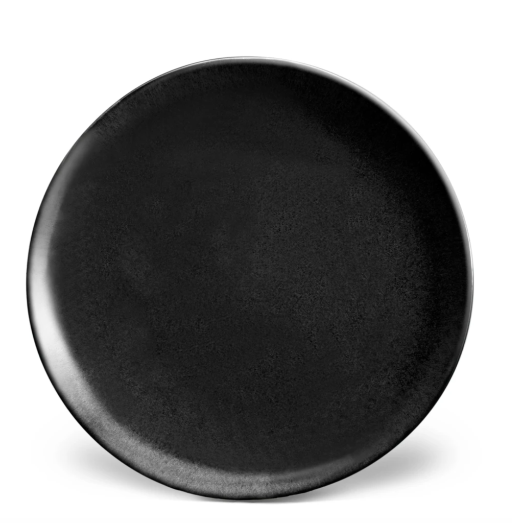 A round, matte black ceramic plate from the Terra Iron Dinnerware collection by L'Objet features a subtle textured finish. Handcrafted and empty, it is photographed from above against a plain white background.