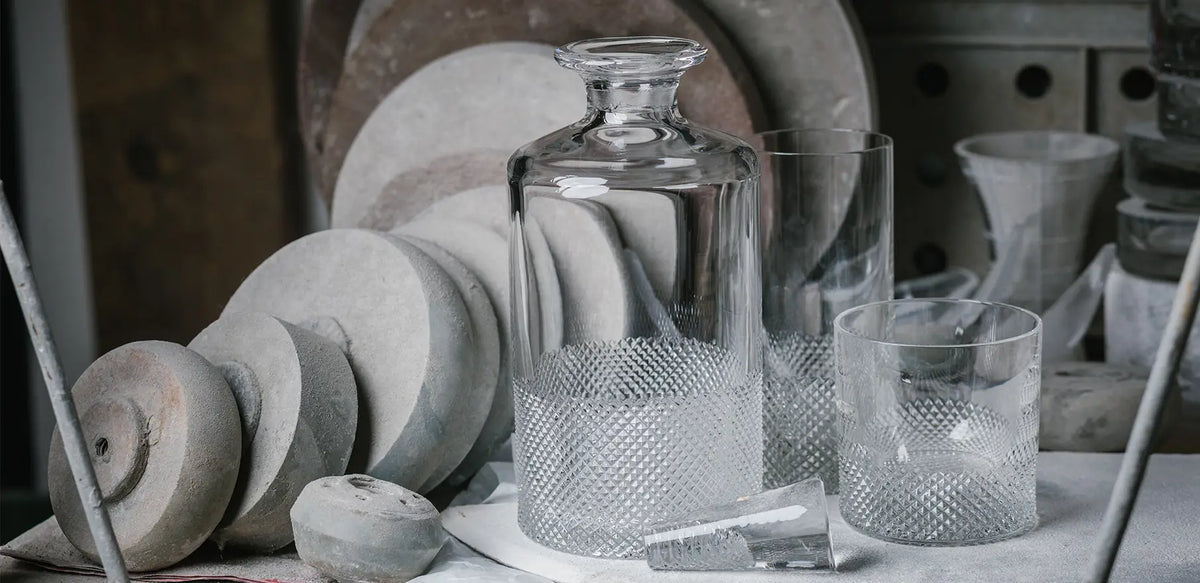 The Richard Brendon Diamond Highball stands on a table in a workshop, surrounded by round gray stone polishing wheels and glass shards.