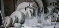 The Richard Brendon Diamond Highball stands on a table in a workshop, surrounded by round gray stone polishing wheels and glass shards.
