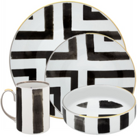 The Sol Y Sombra set by Christian Lacroix x Vista Alegre features ceramic plates, bowl, and mug with bold black geometric brushstrokes on white backgrounds and gold rims—showcasing modern Vista Alegre flair.