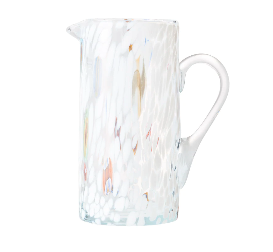 The Kim Seybert Gala Pitcher White is a tall, clear pitcher with a side handle, featuring a white, textured speckled pattern and subtle color accents that highlight the elegance of Murano-style glass.