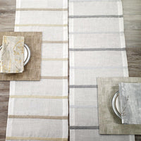 A top-down view of two table settings with Bodrum Metallic Band Silver Table Runners, each featuring a plate, a subtly patterned brown or gray napkin, and a matching rectangular placemat on a wooden table.