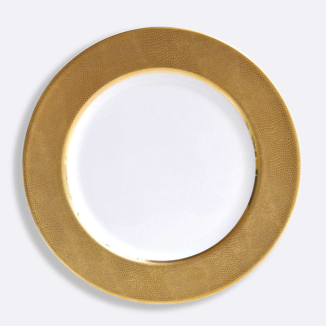 The Sauvage Gold Dinnerware by Bernardaud features a round white Limoges porcelain plate with a wide, embossed gold snake skin rim, displayed on a plain light gray background.