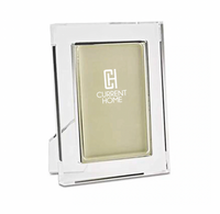 The Tizo Matte Lip Frame Clear is a modern clear rectangular glass or acrylic photo frame with a gold backing and white Current Home logo on the front, standing upright for a chic and elegant display.