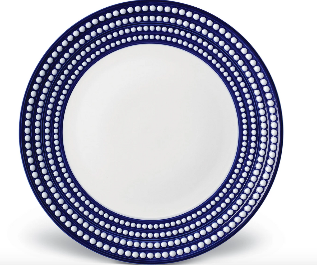 The L'Objet Perlèe Blue Dinnerware features a round white ceramic plate with a wide navy blue rim, accented by concentric circles of evenly spaced white dots along the border.