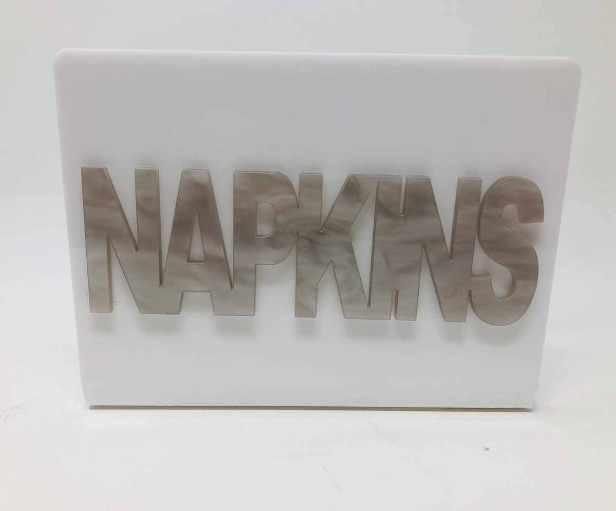 The Eye Candy Acrylic Napkin Holder features bold, marble-patterned "NAPKINS" lettering cut out on the front for a stylish, modern touch.