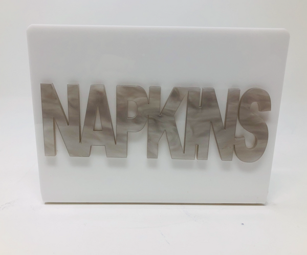 The Eye Candy Acrylic Napkin Holder features bold, marble-patterned "NAPKINS" lettering cut out on the front for a stylish, modern touch.