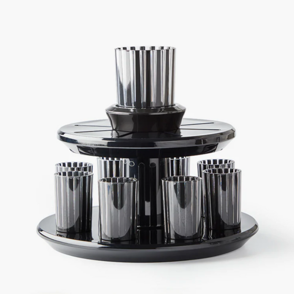 The Apeloig Kiddush Wine Fountain Set features a modern, glossy black two-tiered rotating holder with eight vertically grooved, metallic-finished cups on the lower tier and one cup on top.