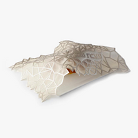 The Apeloig Geometric Challah Cover features a translucent, honeycomb-like lattice draped over a rectangular base with an orange accent beneath, blending modern design with traditional inspiration.