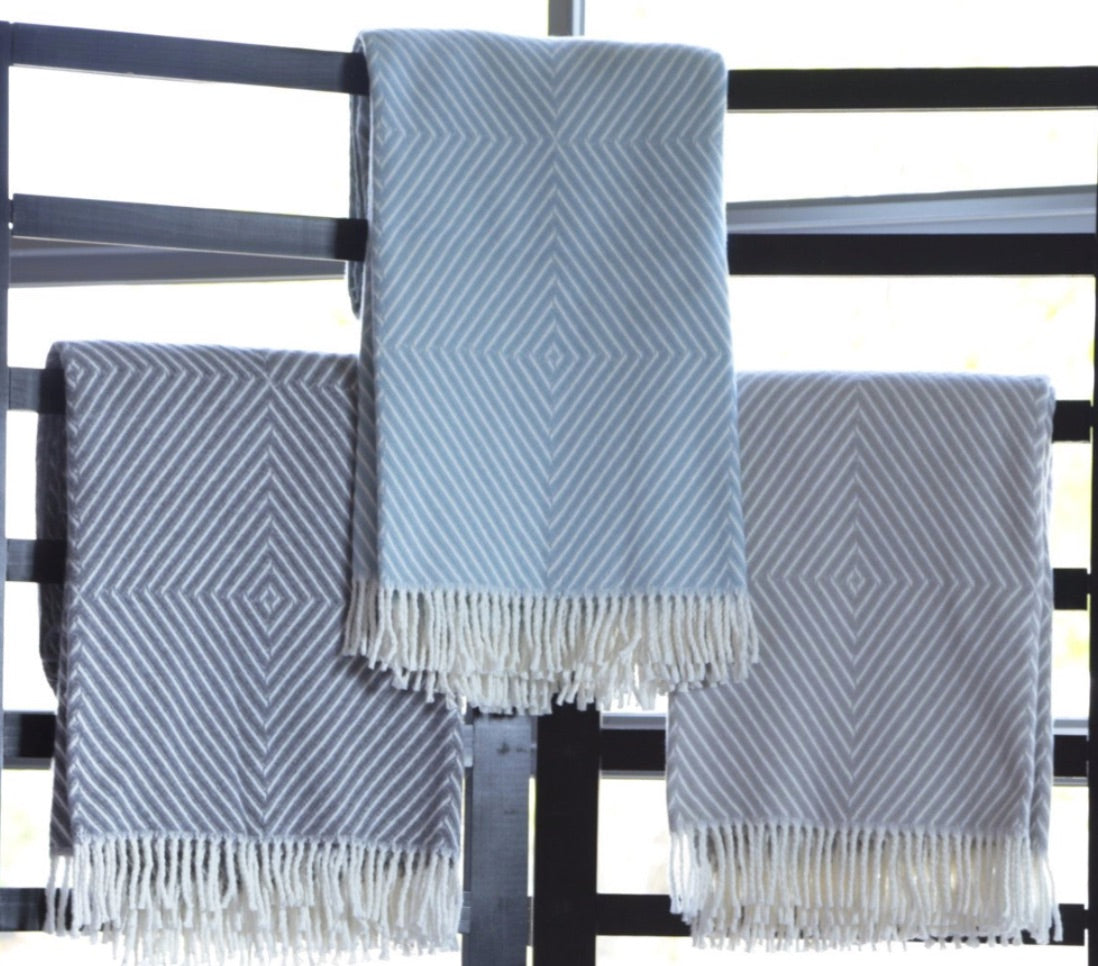 Three A Soft Idea Personalized Throw Blankets with geometric diamond patterns, including a monogrammed grey and white option, hang over a black rail against a bright window background.