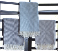 Three A Soft Idea Personalized Throw Blankets with geometric diamond patterns, including a monogrammed grey and white option, hang over a black rail against a bright window background.