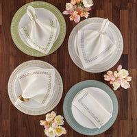Four elegant place settings on a wooden table feature Bodrum Pearls Napkin Navy Set of 4, each paired with white plates with pastel accents, napkin rings, and a nearby bouquet of pink and white flowers.