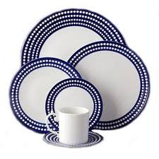 The Perlèe Blue Dinnerware by L'Objet features Limoges porcelain dishes with signature dotted borders, including dinner plates, salad plates, cup, and saucer—all elegantly displayed in blue and white.