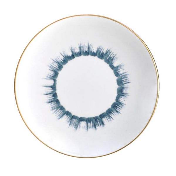 The Marie Daâge Iris 1 Dinnerware by Marie Daâge features a round white Limoges porcelain plate with a thin gold rim and a blue brushstroke-style circular pattern at the center, evoking a ring or sunburst.