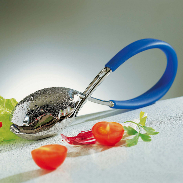 The Casa Bugatti KISS Salad Tong, with its shiny metal finish and blue handle, rests on a light surface beside cherry tomatoes, red chili pepper pieces, parsley, and lettuce—a stylish accessory for summer entertaining.