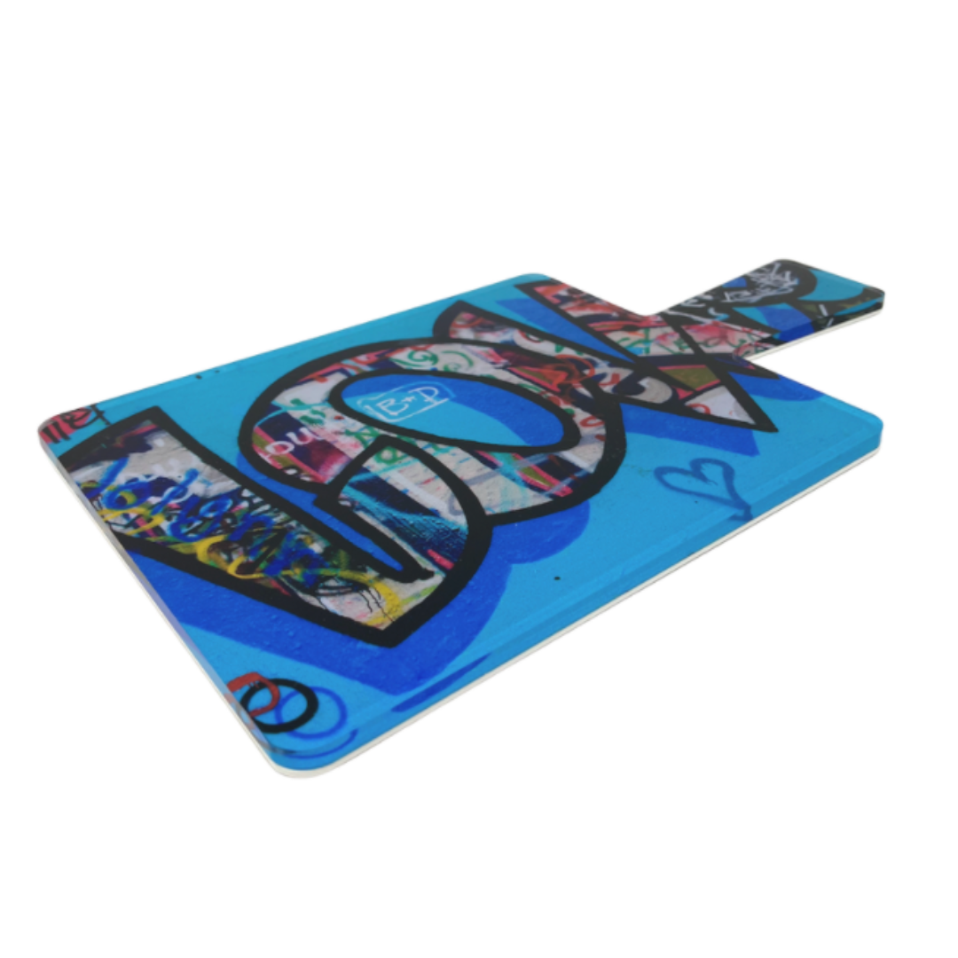 The Eye Candy Love Charcuterie Board is a rectangular serving board with a handle, featuring vibrant graffiti art on a blue background and the bold word "LOVE" across the surface.