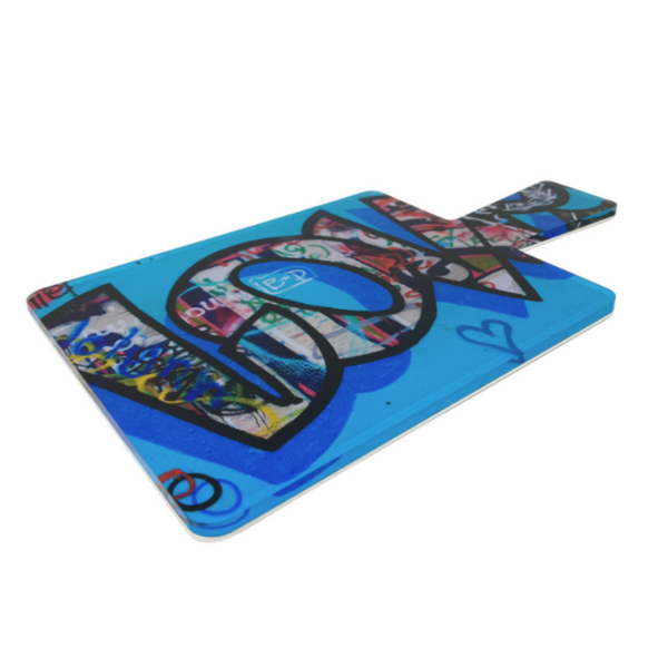 The Eye Candy Love Charcuterie Board is a rectangular serving board with a handle, featuring vibrant graffiti art on a blue background and the bold word "LOVE" across the surface.