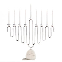 The Coluna Menorah Carrara Marble & Silver by Anna New York features a modern, looped silver metal design paired with an elegant Italian Carrara marble base. It holds eight white candles and is shown against a white background.