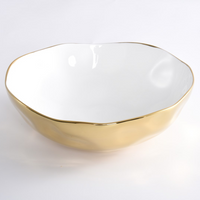 The PAMPA BAY Moonlight Bowl is a white porcelain serveware bowl featuring an uneven rim and a shiny gold exterior, shown on a white background.