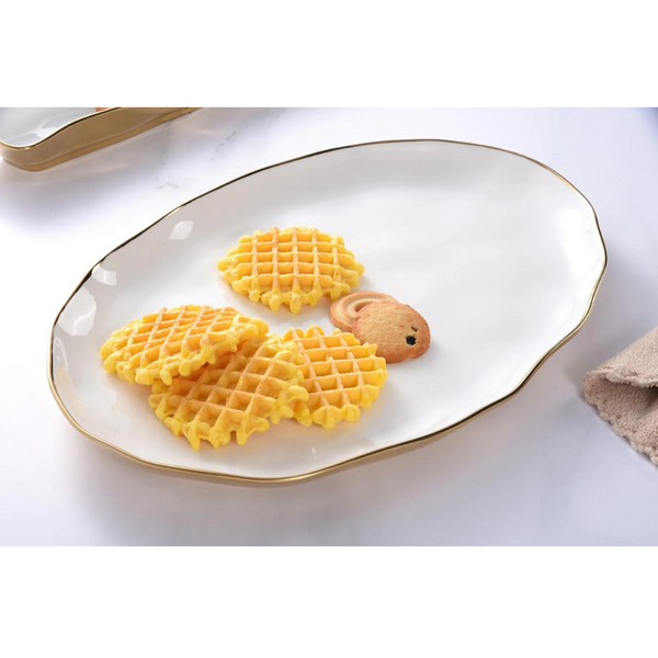 Four golden waffles and a teddy bear-shaped cookie rest on the Moonlight Oval Tray by PAMPA BAY, a white porcelain platter with wavy edges and an elegant gold titanium trim.