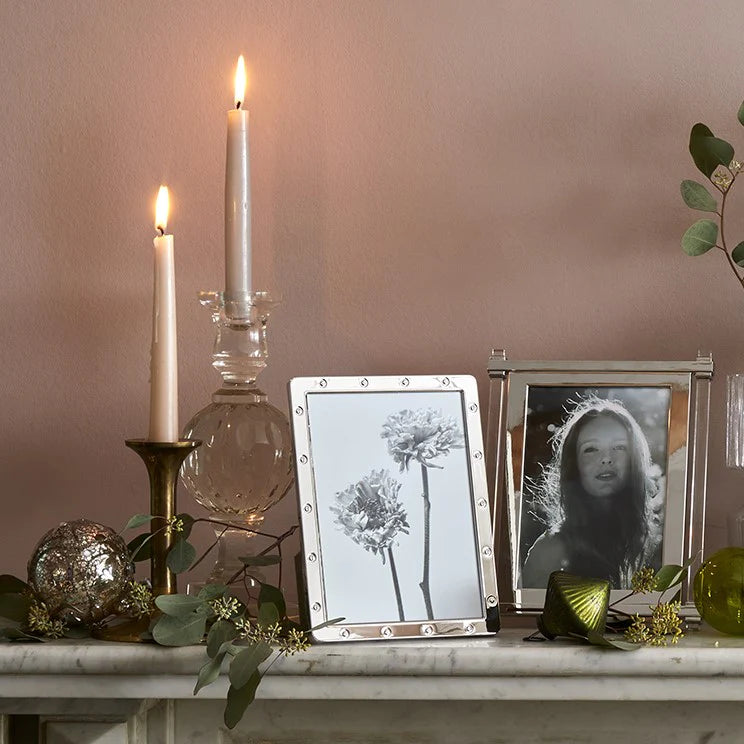 A marble mantel adorned with candles, greenery, ornaments, and two photo frames—including the Addison Ross Locket Frame Silver—sits against a soft blush wall for an elegant scene.
