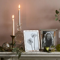 A marble mantel adorned with candles, greenery, ornaments, and two photo frames—including the Addison Ross Locket Frame Silver—sits against a soft blush wall for an elegant scene.