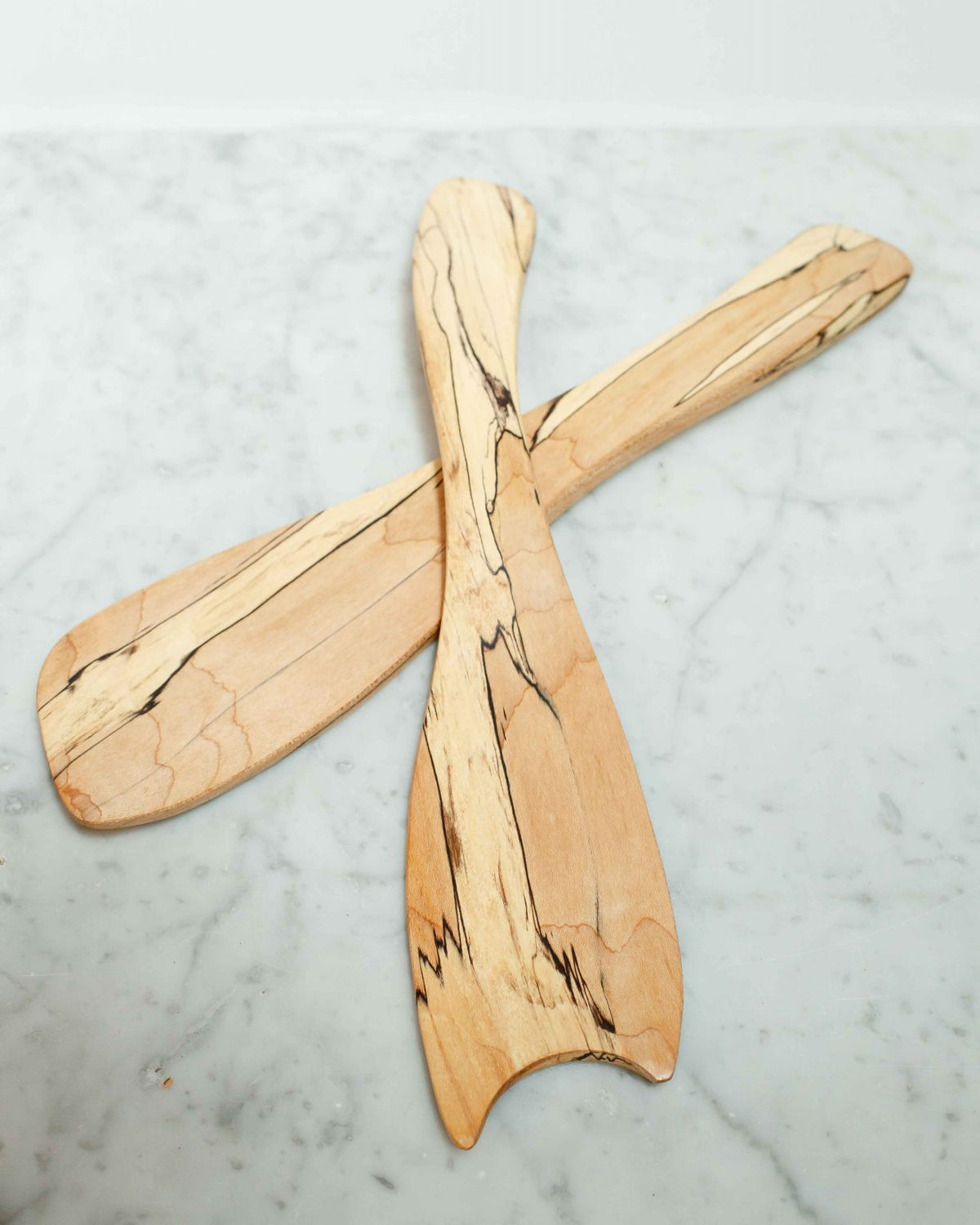 Two Spalted Maple Rustic Salad Tossers by Peterman, featuring dark grain patterns, are crossed on a white marble surface.