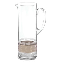 The Truro Platinum Pitcher by Michael Wainwright is a clear glass, tall and cylindrical with a curved handle, spout, and an elegant band of oval patterns near the base for a refined look.