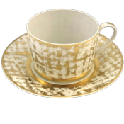 The Royal Limoges Tweed White & Gold Dinnerware teacup features a handle and matching saucer, both adorned with a white and gold geometric design—an elegant addition to any dinnerware collection.
