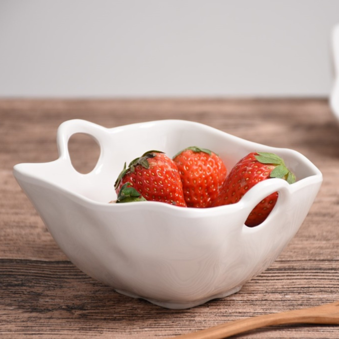 The PAMPA BAY Ivy Melamine Snack Bowl, a BPA-free, shatterproof white bowl with decorative handles, holds four fresh strawberries and sits on a wooden surface against a neutral background.