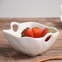The PAMPA BAY Ivy Melamine Snack Bowl, a BPA-free, shatterproof white bowl with decorative handles, holds four fresh strawberries and sits on a wooden surface against a neutral background.